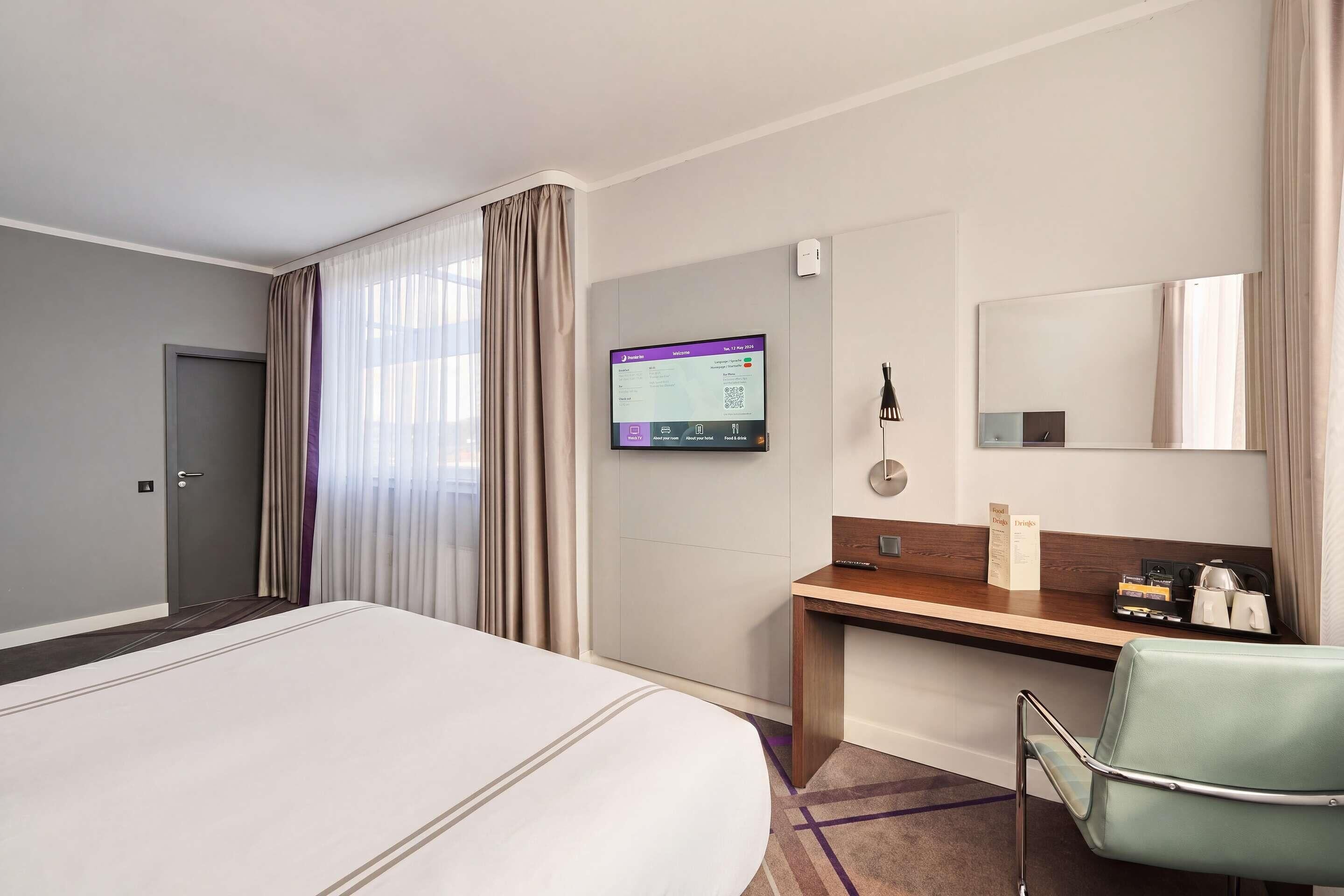 Una habitación de hotel con cama, escritorio, silla, televisión y puerta.