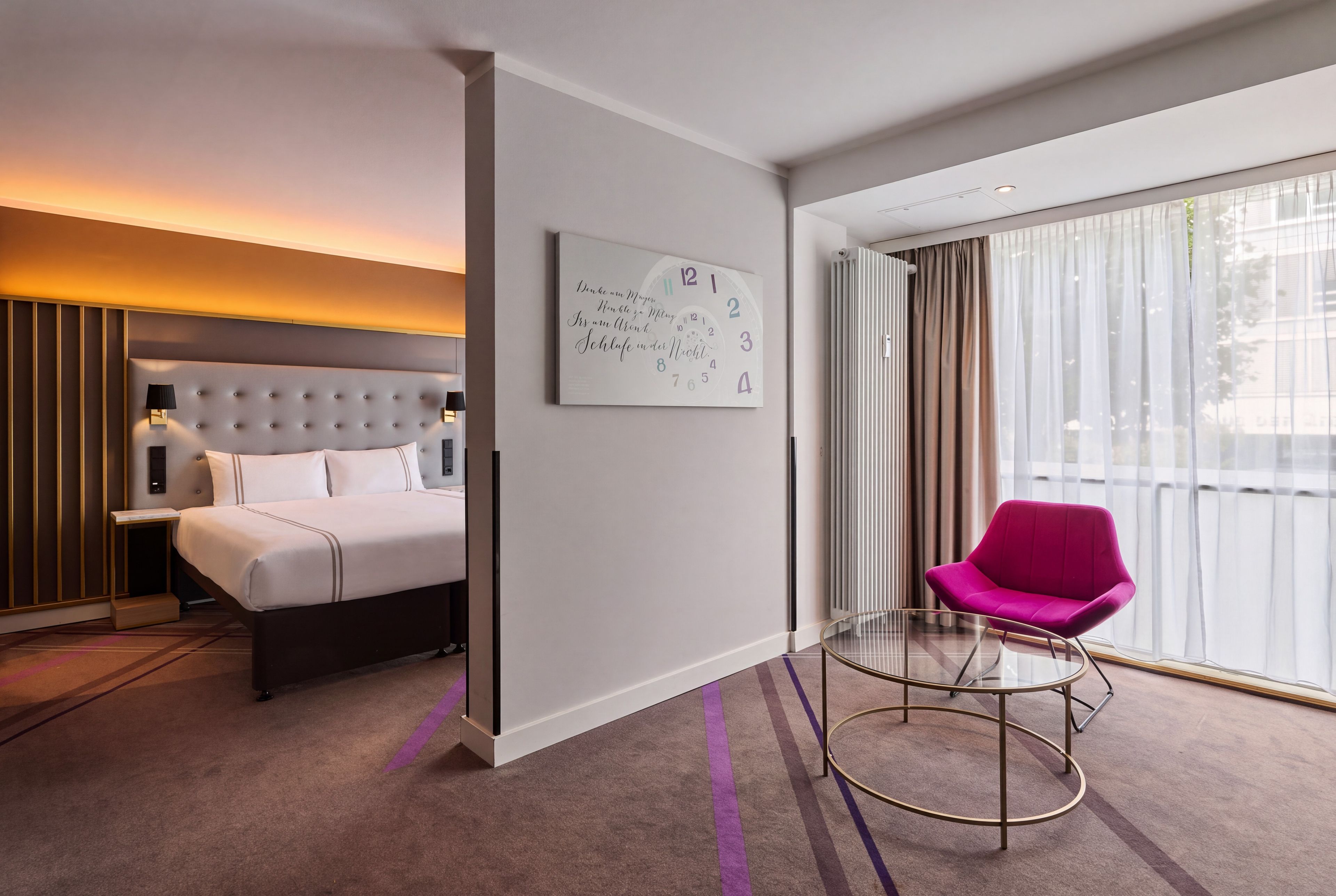 Una habitación de hotel moderna con una cama, una silla, una mesita de noche, un reloj de pared y un ventanal con cortinas.