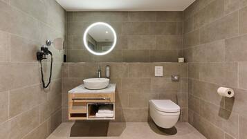 A modern bathroom with a built-in sink, a toilet, a towel rack, and a mirror with a circular light.