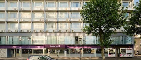 Un hôtel à plusieurs étages, reconnaissable à son grand panneau « Premier Inn », doté de climatiseurs et orné d’un arbre devant l’entrée.