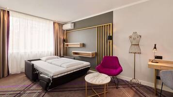 A hotel room with a bed, a desk, a chair, a small table, and a decorative mannequin.