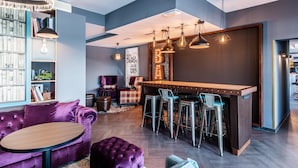 A modern interior with a bar area, seating, and a bookshelf. - Premier Inn Saarbrücken City Centre (Saarbrucken)