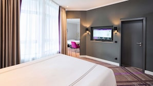 A hotel room with a bed, a TV mounted on the wall, a door, and a window with curtains. - Premier Inn Saarbrücken City Centre (Saarbrucken)