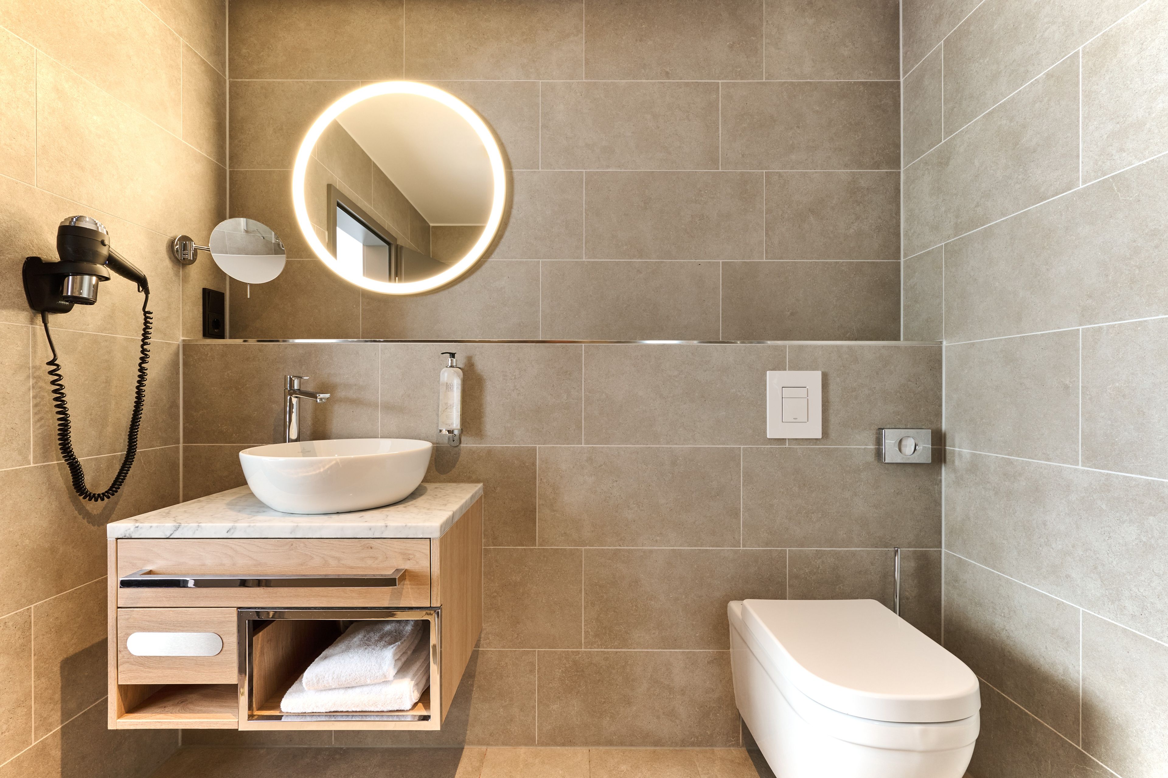 A modern bathroom with a white sink, a mirror with a light, a hairdryer, and a toilet.