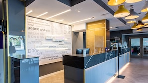 A modern hotel reception area with a marble counter, a large wall with motivational phrases, and pendant lighting. - Premier Inn Saarbrücken City Centre (Saarbrucken)