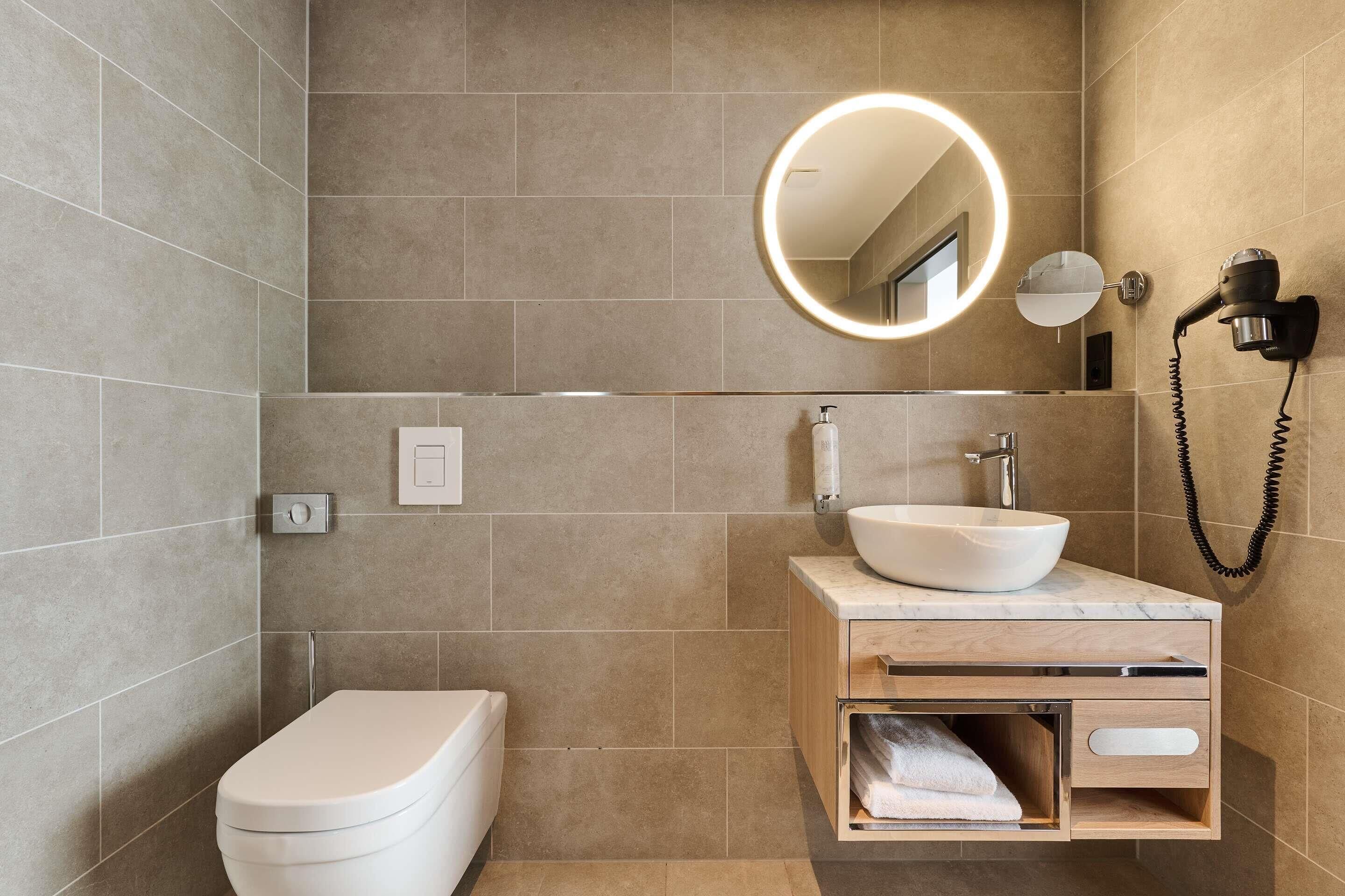 A modern bathroom with a toilet, sink, vanity, mirror, and hairdryer.