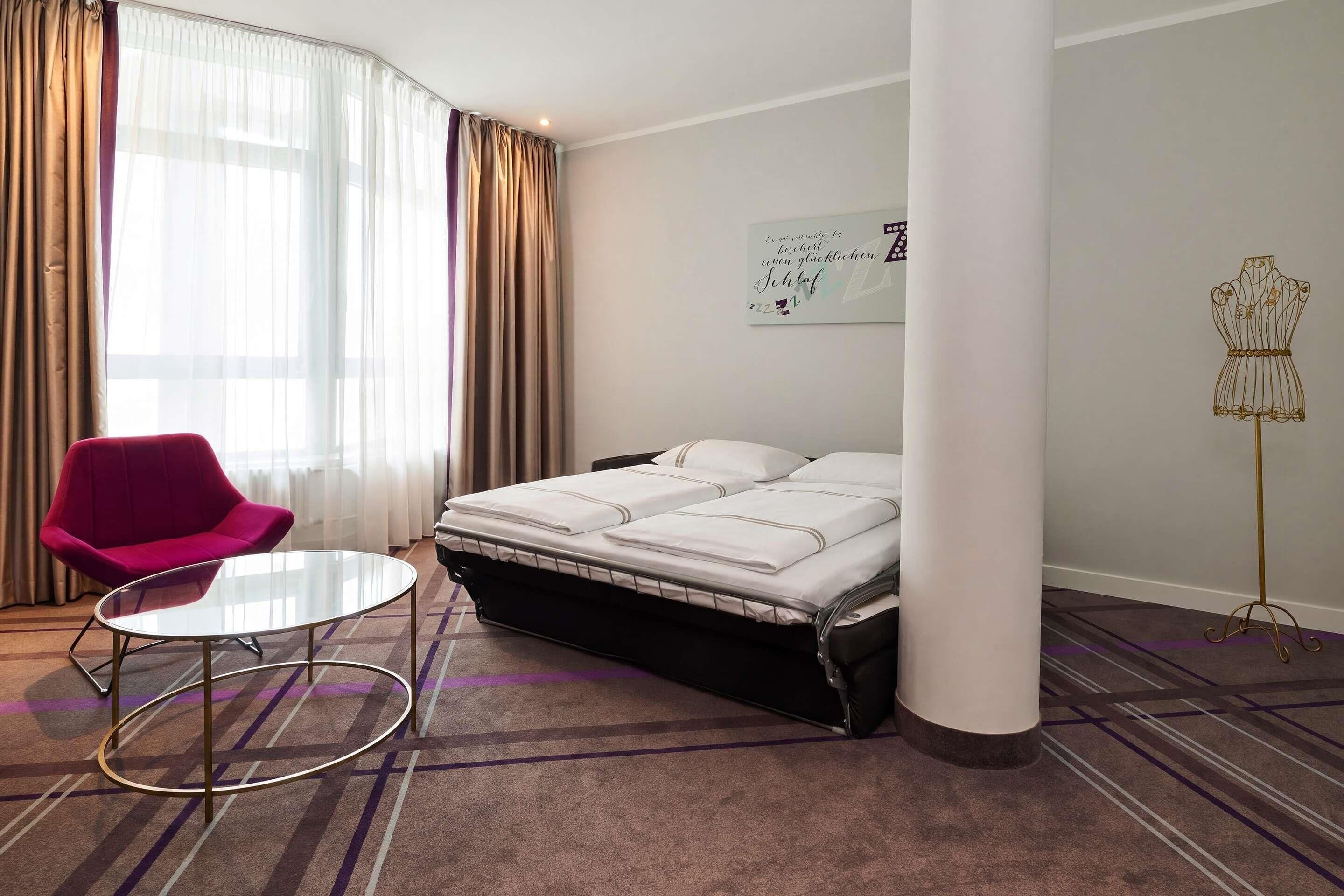 Una habitación de hotel con una cama, una silla, una mesa y un maniquí.