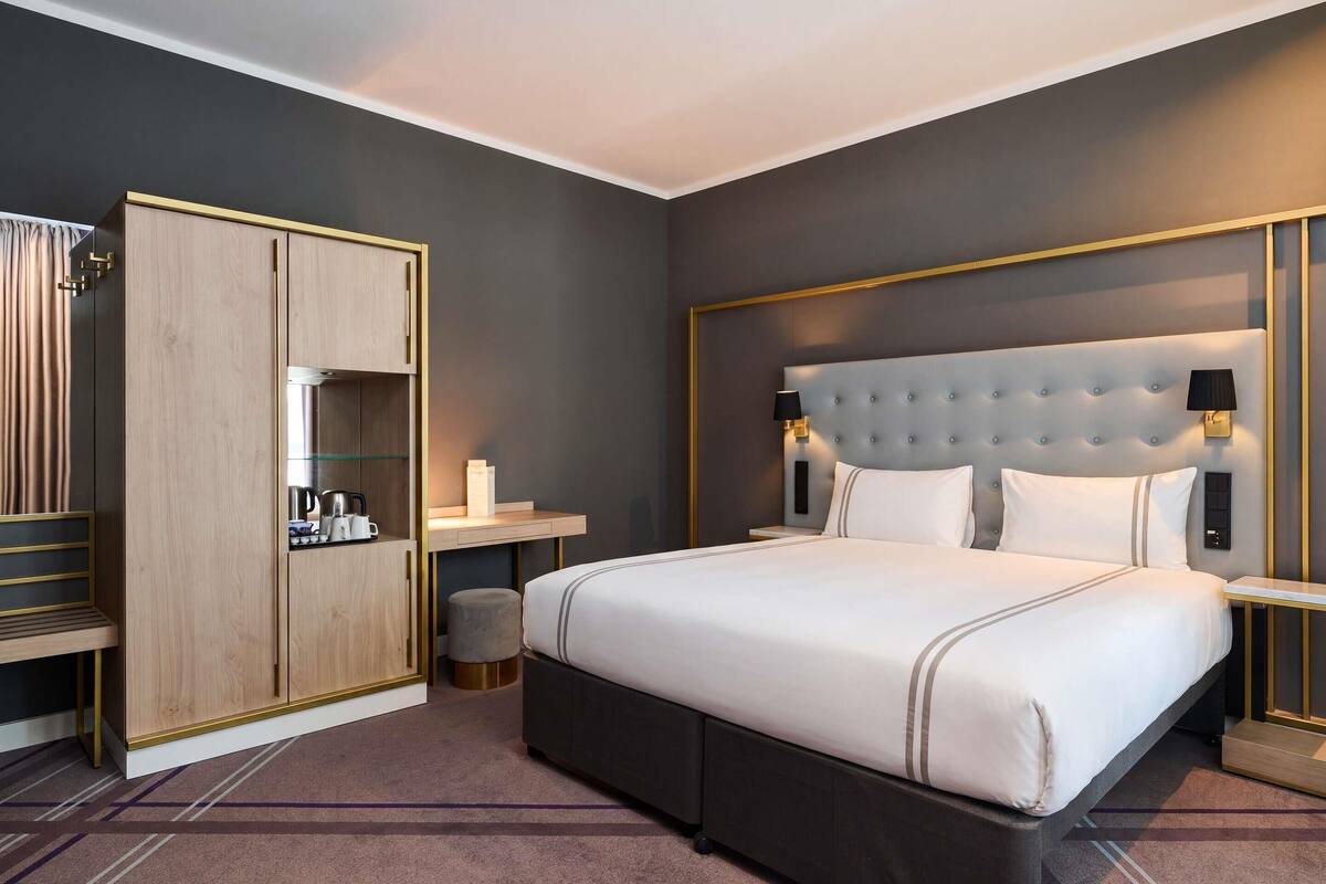 Et moderne hotelværelse med en stor seng, et garderobeskab, et natbord og en lille skammel.