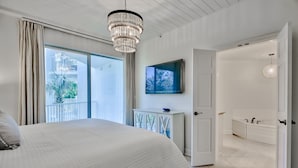 Ein Schlafzimmer mit einem großen Bett, einer Kristallleuchter, einem Fernseher und Blick auf einen Balkon.