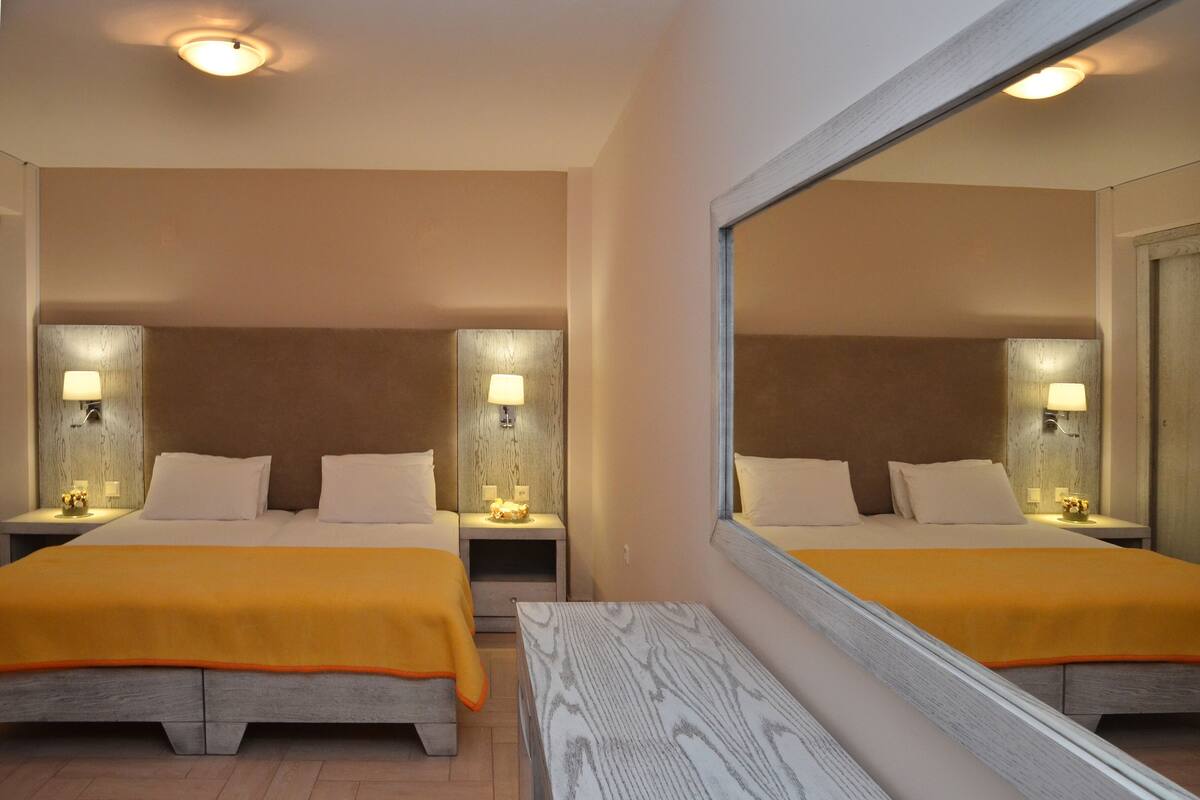 A hotel room with two beds, each with a wooden headboard, a nightstand, a lamp, and a mirror.