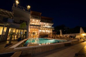 A modern hotel with a swimming pool, outdoor seating, and a well-lit facade. - Aria Hotel Skiathos (Skiathos)