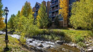 A multi-story building with balconies, surrounded by autumn-colored trees and a stream. - 2 Bedroom Ski in Condo Only One Block From Historic Downtown, Shopping, Restaurants and Entertainment (Breckenridge)