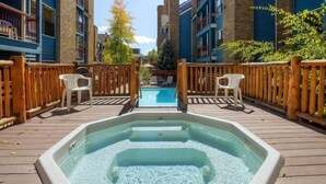 A hot tub on a wooden deck with a pool in the background, surrounded by a wooden fence and chairs. - 2 Bedroom Ski in Condo Only One Block From Historic Downtown, Shopping, Restaurants and Entertainment (Breckenridge)