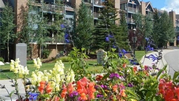 A multi-story hotel with balconies, surrounded by lush greenery and colorful flowers. - 2 Bedroom Ski in Condo Only One Block From Historic Downtown, Shopping, Restaurants and Entertainment (Breckenridge)