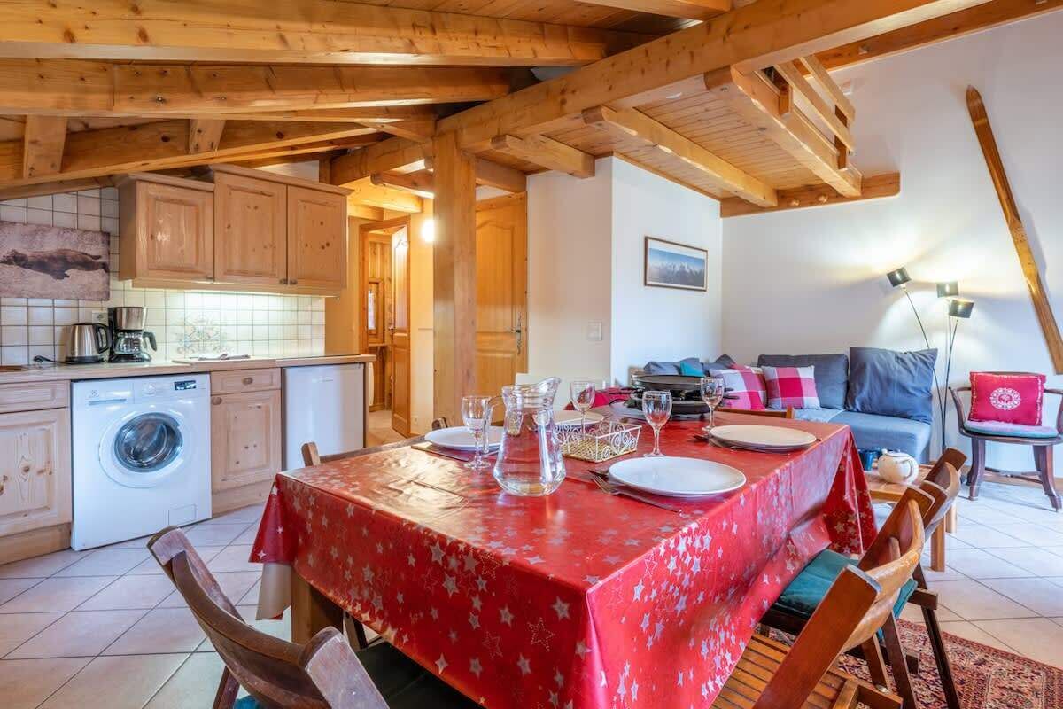 A cozy kitchen with wooden beams, a washing machine, and a dining area with a red tablecloth.