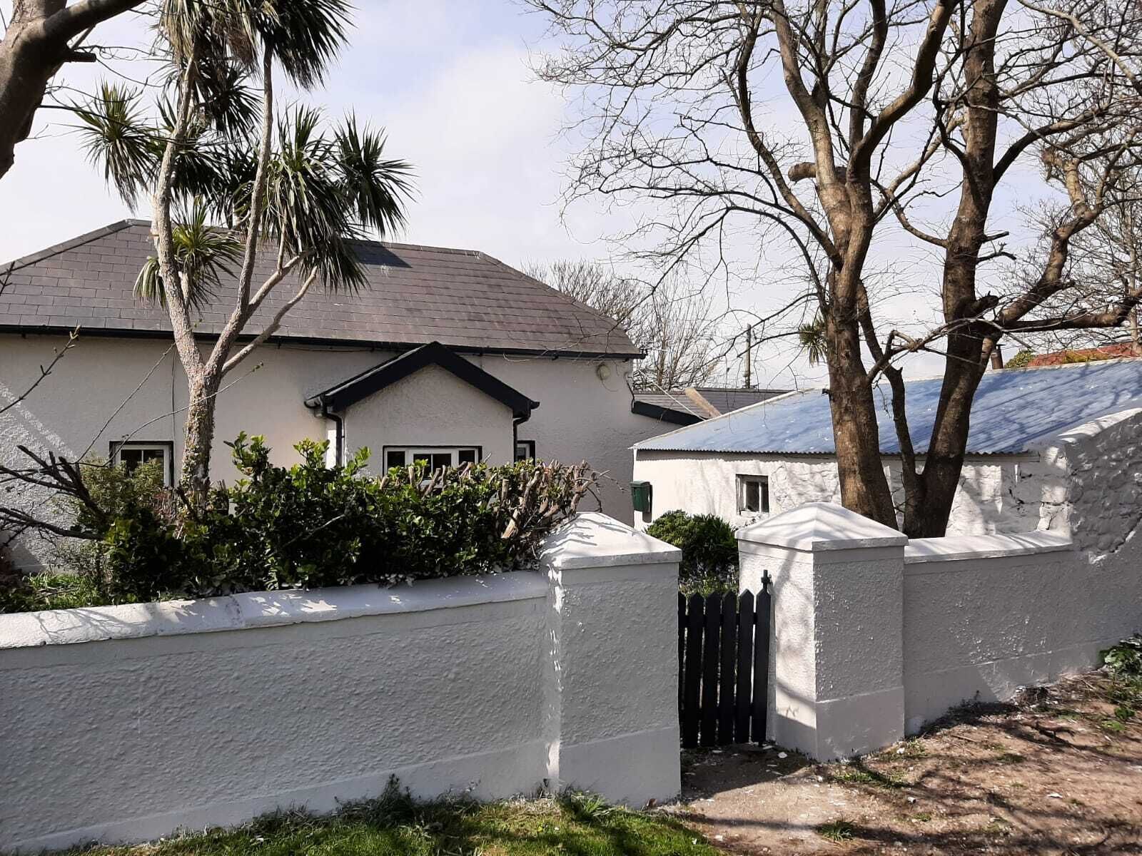 A single-story house with a gabled roof, surrounded by a white wall and a wooden fence.