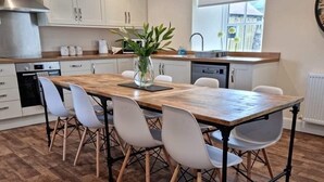 Eine moderne Küche mit einem Holztisch, weißen Stühlen und einer Blumenvase.