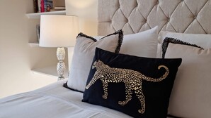 Ein ordentlich gemachtes Bett mit einer gesteppten Kopfteil, einer Nachttischlampe und einem Regal mit Büchern und einer Pflanze.