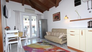 A living room with a sofa, a dining table with chairs, a colorful rug, and a kitchen area with cabinets and a refrigerator. - Apartment Ala (Rovinj)