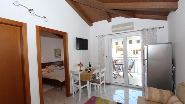 A room with a bed, a dining table with chairs, a sofa, a refrigerator, and a television on the wall. - Apartment Ala (Rovinj)