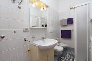A bathroom with a white sink, a mirror, a toilet, and a shower. There are two towels hanging on the wall. - Apartment Ala (Rovinj)