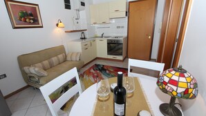 A small kitchen with a stove, oven, and sink. There is a dining table with a bottle of wine and glasses. A colorful lamp is on the table. - Apartment Ala (Rovinj)