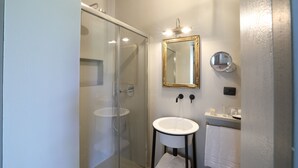 A modern bathroom with a glass shower enclosure, a white sink, and a gold-framed mirror. - Appartamento Monforte 4 in Villa (Barolo)