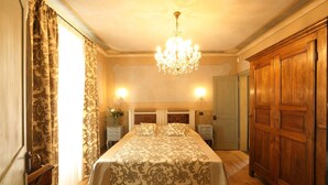 A hotel room with a large bed, wooden wardrobe, chandelier, and two bedside lamps. - Appartamento Monforte 4 in Villa (Barolo)