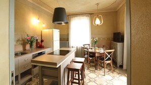 A compact kitchen with a central island, a dining area with wooden chairs, and a TV in the corner. - Appartamento Monforte 4 in Villa (Barolo)