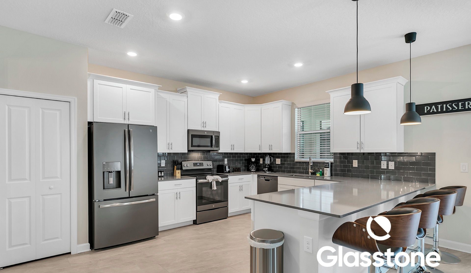Una cocina moderna con gabinetes blancos, electrodomésticos de acero inoxidable y una isla central con taburetes de bar.