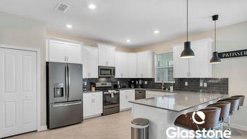 Una cocina moderna con gabinetes blancos, electrodomésticos de acero inoxidable y una isla central con taburetes de bar.