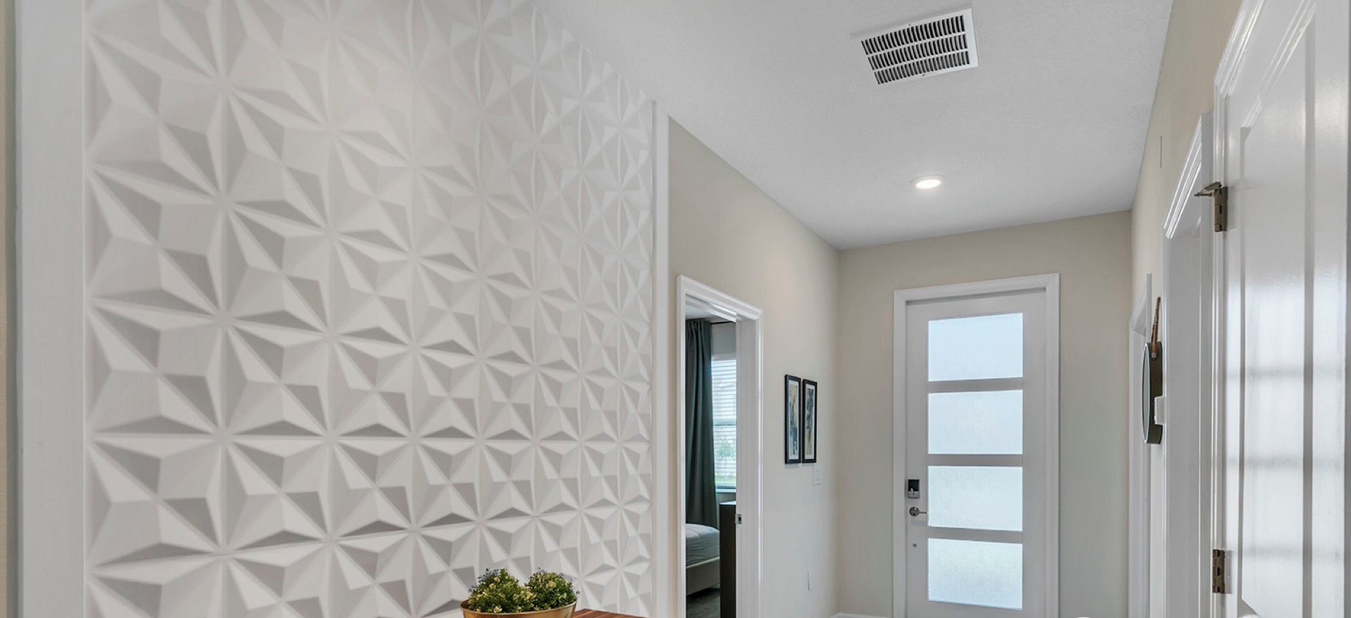 A hallway with a geometric-patterned wall, a wooden bench with a bowl of plants, and a door with frosted glass panels.