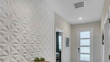 A hallway with a geometric-patterned wall, a wooden bench with a bowl of plants, and a door with frosted glass panels.