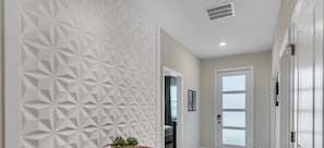 A hallway with a geometric-patterned wall, a wooden bench with a bowl of plants, and a door with frosted glass panels.