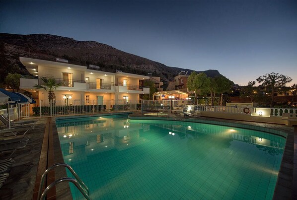A swimming pool with a view of a multi-story building and a mountain in the background. - Adonis Studios Koutouloufari (Hersonissos)