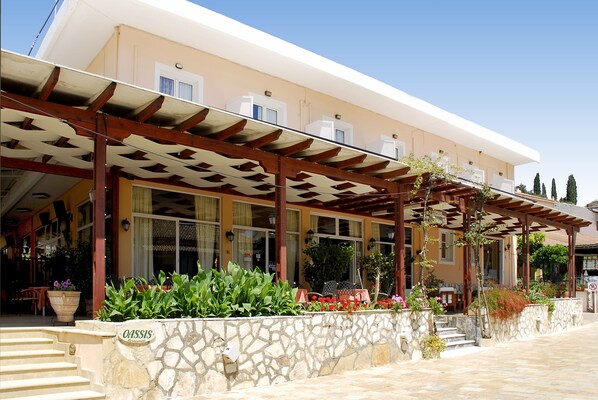A building with a stone facade, a covered outdoor area with wooden beams, and a sign that reads "OASIS Restaurant". - Kassiopi Melina Oasis Hotel (Corfu)