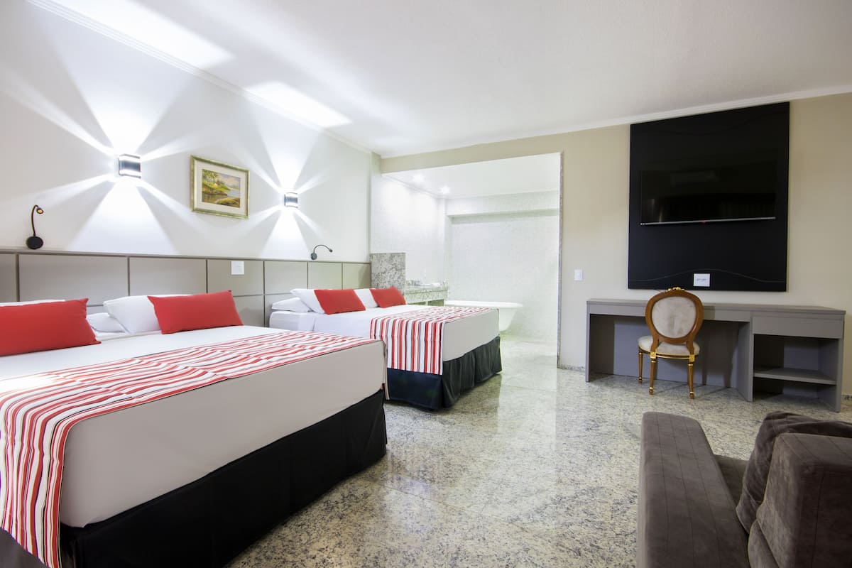 A hotel room with two beds, a desk, a chair, and a TV.