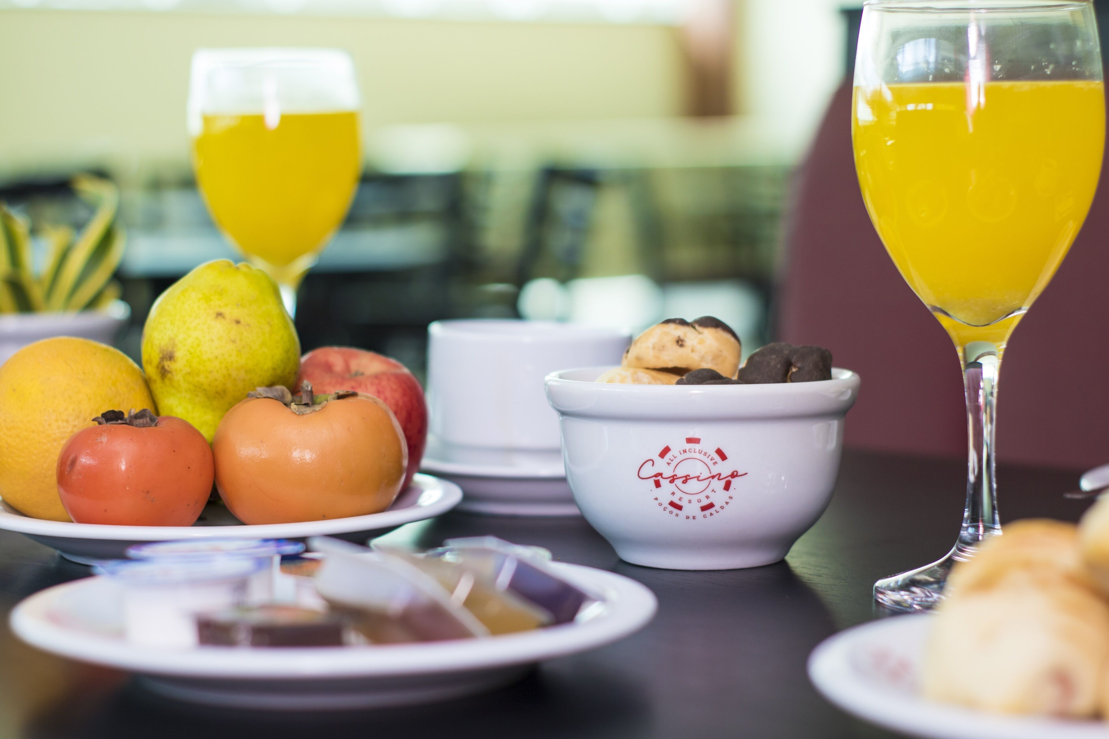 A table with fruits, a glass of orange juice, a bowl of cookies, and a teapot.