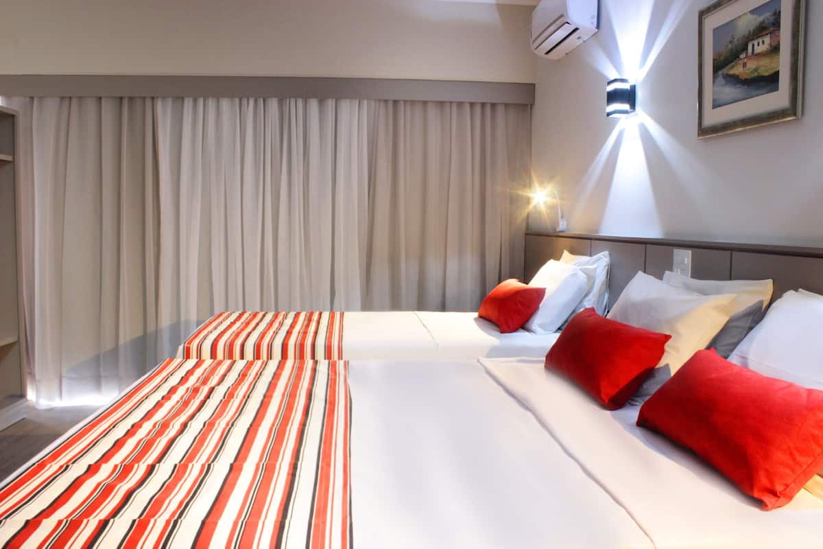 A hotel room with a large bed, striped bedding, and red pillows.
