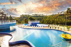 Una piscina con tobogán, sillas de descanso y una palmera al fondo.