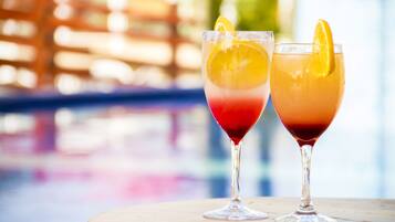 Two cocktails on a wooden table with a blurred background of a pool and a wooden fence.