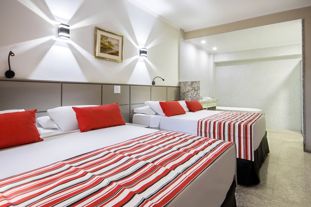 A hotel room with two beds, each with red and white bedding, a headboard, and a nightstand with a lamp.