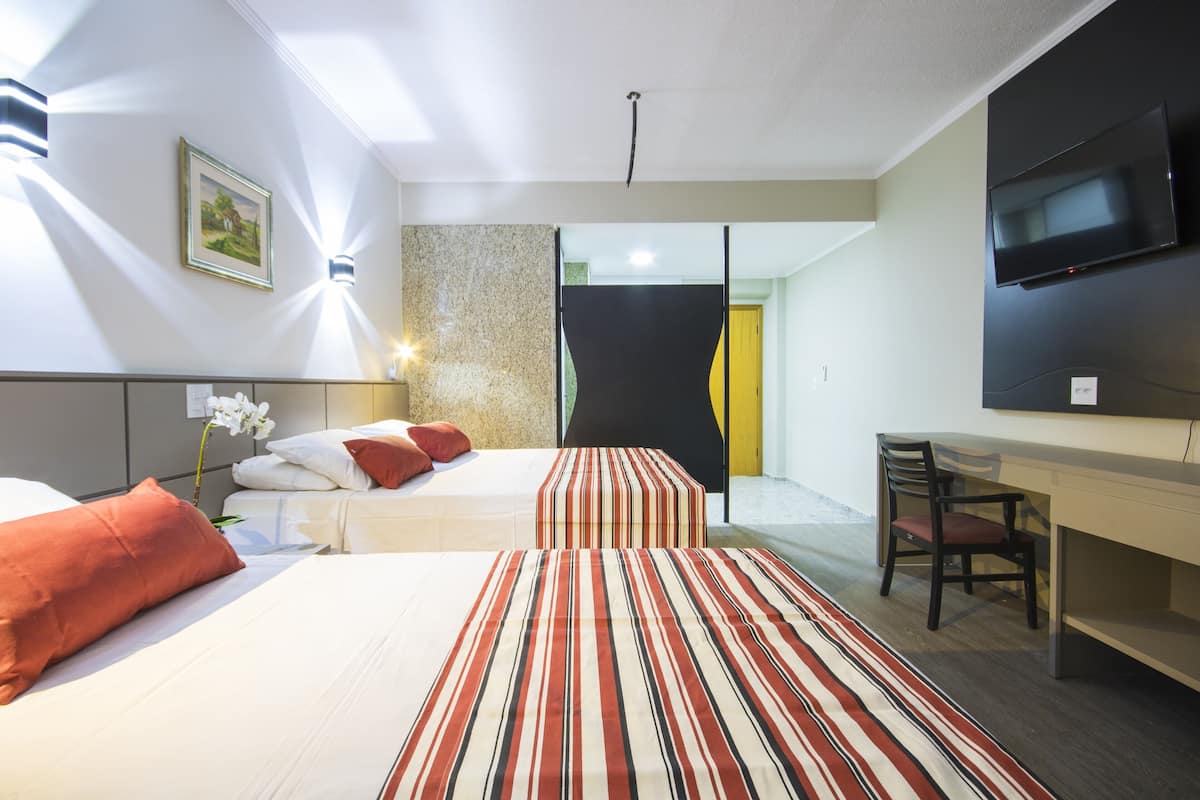 A hotel room with two beds, a desk, a chair, a TV, and a painting on the wall.