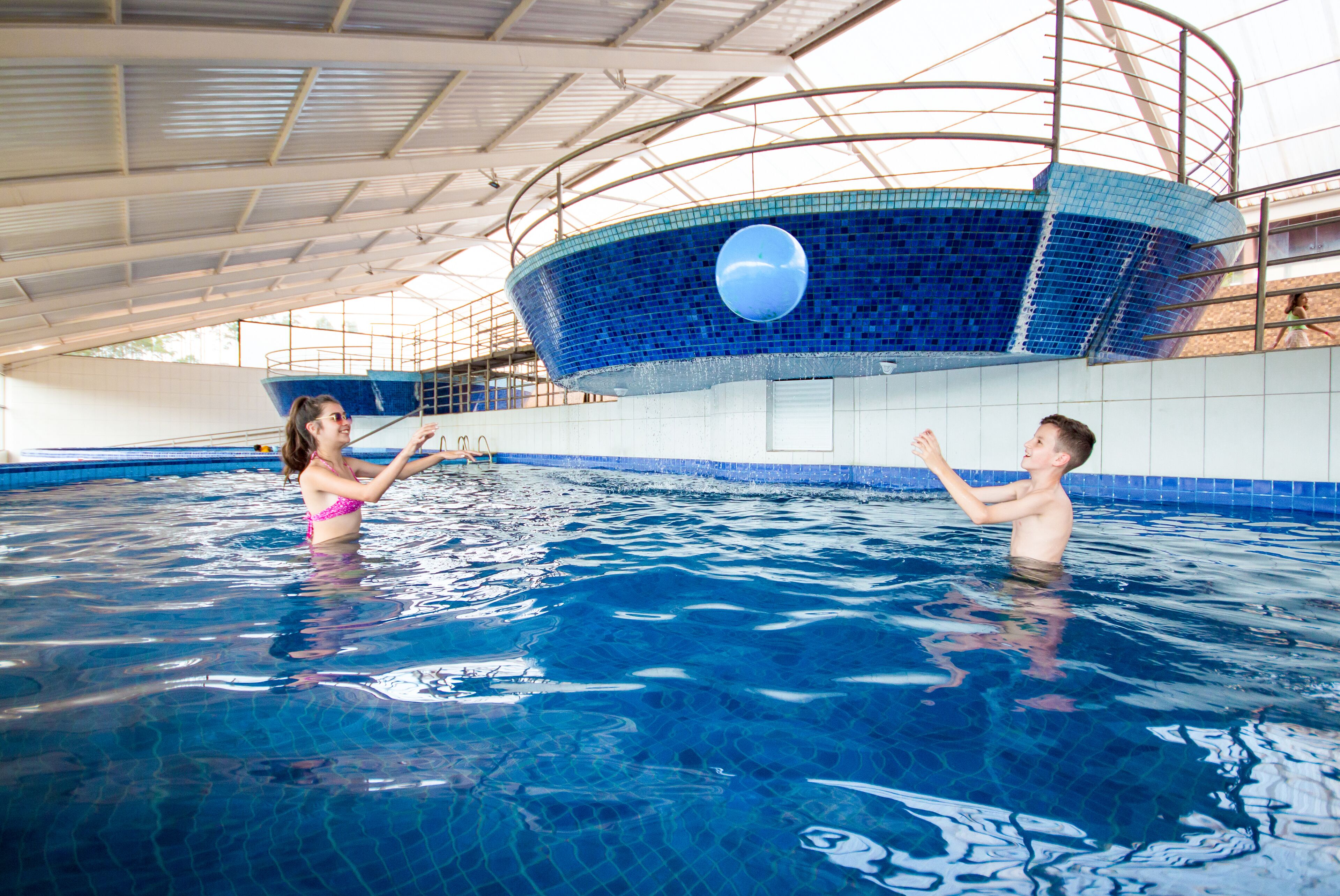 An indoor swimming pool with a blue tiled wall and a large circular window.