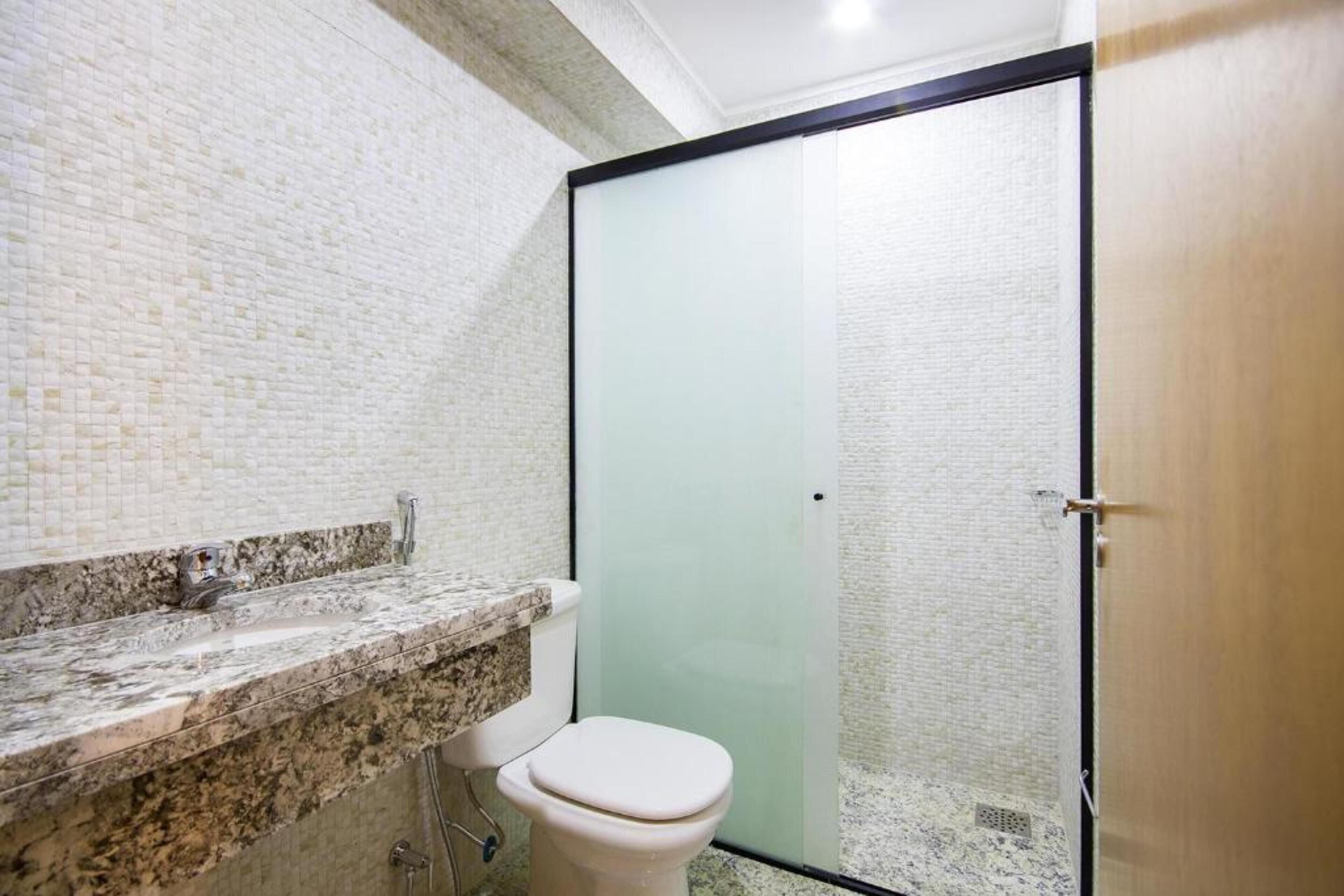 Un baño con lavamanos de mármol, inodoro y cabina de ducha con mampara de vidrio.
