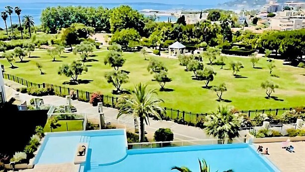 Ein Poolbereich mit Meerblick und ein angelegter Garten mit Bäumen und einem Gazebo.