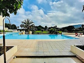 A swimming pool with a tiled deck, palm trees, and a distant view of hills.