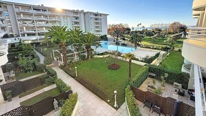 Ein Hotelinnenhof mit Swimmingpool, Palmen und einem gepflegten Rasen.