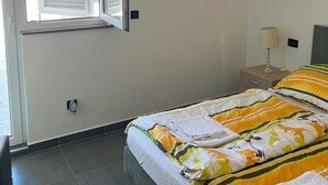 A bedroom with a bed, a nightstand, a lamp, and a window with blinds. - Villa Pina TOP****Apartment Nicos at the see 2-4 persons (Tisno)