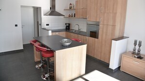A modern kitchen with wooden cabinets, a central island with stools, a stainless steel range hood, and a built-in oven. - Villa Pina TOP****Apartment Nicos at the see 2-4 persons (Tisno)